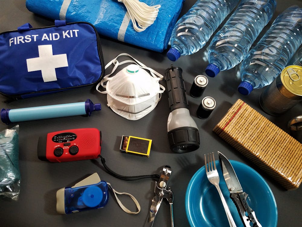 Emergency go-bag supplies laid out: first aid kit, water bottles, flashlight, batteries, radio, and other survival essentials