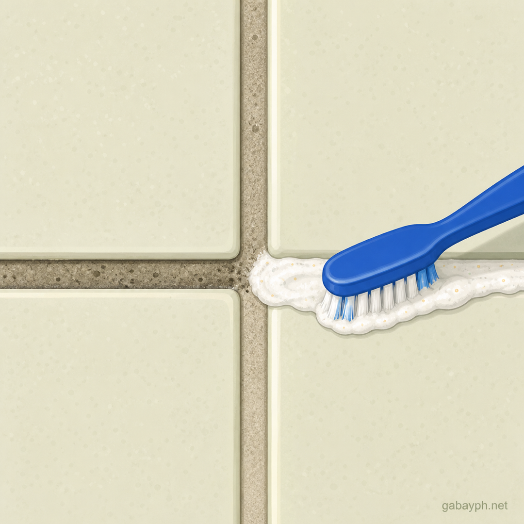 Old toothbrush applying white paste to grimy grout lines