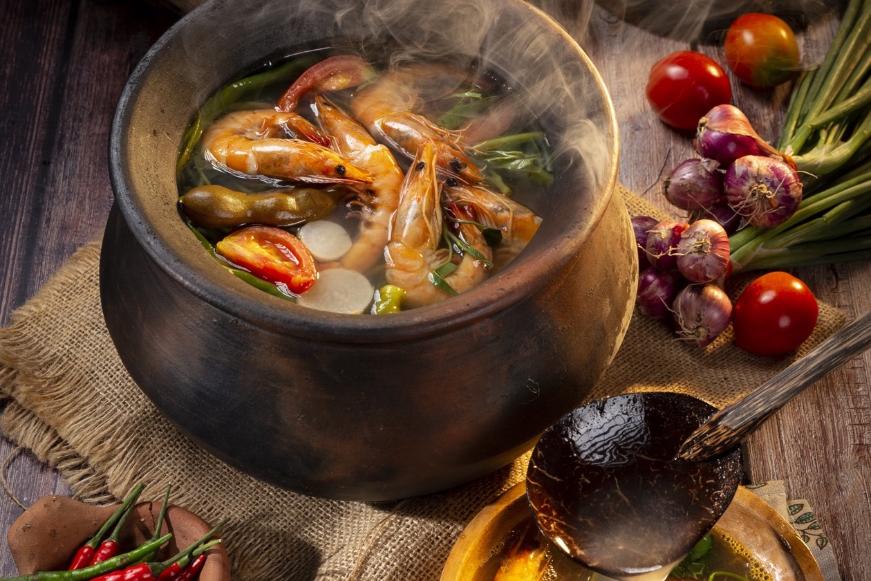 Sinigang na hipon steaming in a clay pot with fresh vegetables and tamarind